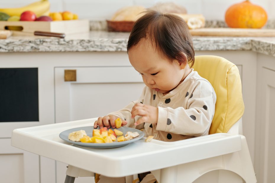 Bebé comiendo con las manos fruta fresca en su trona